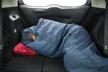 寝袋を使って車中泊をする男性