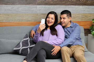 Latino couple of man and woman spend time together, see photos on their cell phone and make...