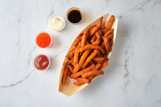 top shot of sweet potato fries in a container with 4 kinds of sauce on a marble table