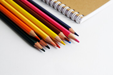 Obraz premium colored pencils against the background of a desk, notebook, white wall