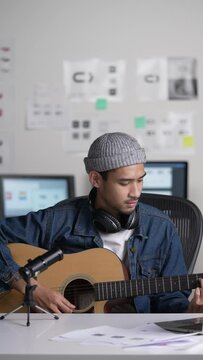 Young Asian male graphic designer blogger influencer playing guitar talking looking at camera while shooting education tutorial vlog training filming video course for social media at studio.