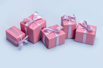 A set of gift boxes wrapped in pink paper tied with a lilac satin ribbon. Blue background, studio shot.
