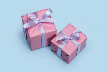 Gift boxes wrapped in pink paper, decorated with lilac satin ribbon. Blue background, copy space.