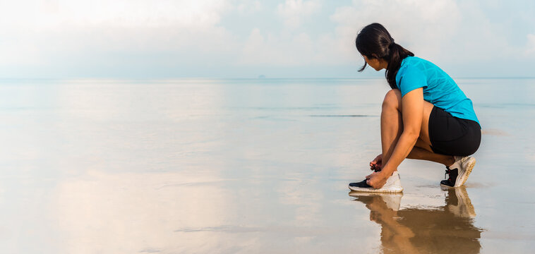 Woman runner in sitting and preparing her running shoe for outdoor exercising run at sea beach in the morning. Panorama image.