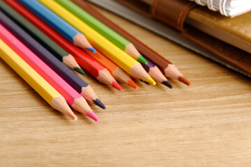 colored pencils against the background of a desk, notebook, white wall