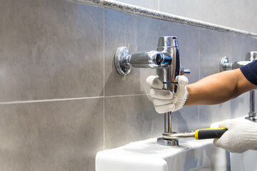 Hand of handyman or plumber is using a wrench to fix or repair leaking water pipes, faucets or valves in toilet bowls and sinks in restroom or bathroom