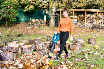 Young woman with her electric blower making piles of dead leaves to clean up the garden