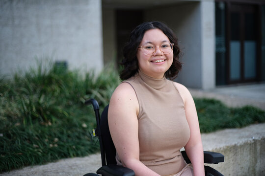 Smiling woman with a disability sitting in a wheelchair outside with grass and plants behind her