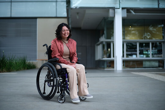 Smiling Asian woman with a disability sitting in a wheelchair outside
