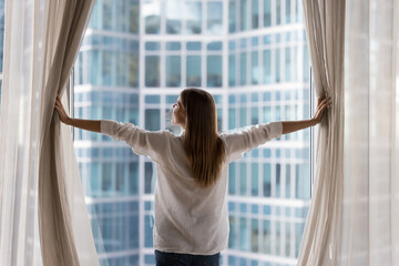 Rear view young woman standing indoors, looking out panoramic window of luxury modern apartment or...