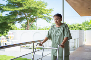 Old elderly disabled Asian patient or pensioner using walker to practice to walk in nursing home in hospital. Senior people lifestyle activity recreation. Health care physical therapy