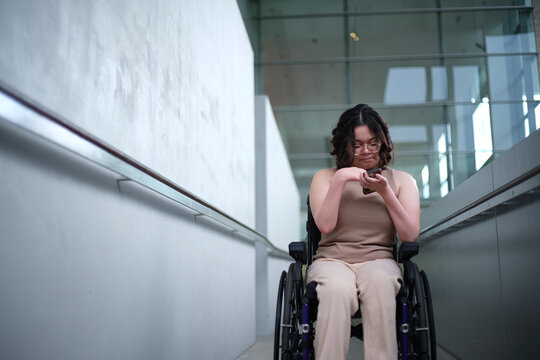 Smiling woman with a disability sitting in a wheelchair looking down at her mobile phone