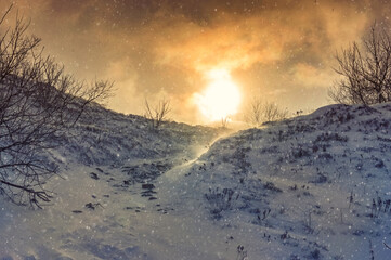 Sunset during heavy snowfall in the mountains. The clouds parted for a few seconds, revealing the winter sun. Dirt rocky road covered with snow