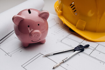 Savings and costs. Yellow safety helmet and pink piggy bank with drawings close-up