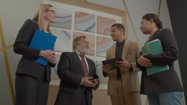 Friendly handsome bearded senior male executive communicating with diverse African American business partners with help of charming female interpreter, discussing business matters at office.