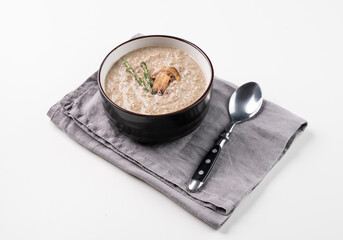 Cream soup of champignons with thyme in a ceramic bowl on a white background with spoon.