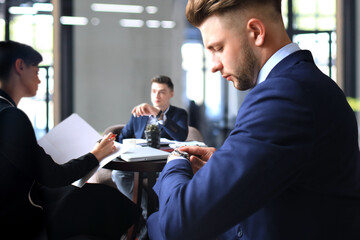 Businessman looks at his wrist watch checking the time. Businessperson sitting a meeting and working at background