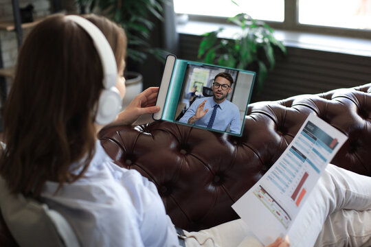 Woman in headphones lying on sofa speak talk on video call with colleagues on online briefing on digital tablet. Transparent modern touchpad of the future concept - Powered by Adobe