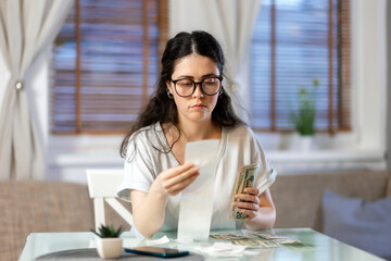 Planning of expenses. Portrait of pensive caucasian young woman accounting cash and paper receipt. Concept of payment of utilities, tax return and savings
