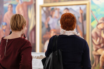 Cultural education. Rear view of women visiting excursion in museum. Defocused paintings in...