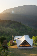 nature camping tent on mountain and holiday relax camp ground in natural tree forest on morning or evening with big buddha background in wat phra thart pha sorn kaew at khao kho phetchabun in thailand