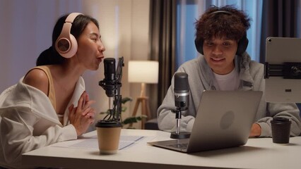 Young happy Asian couple wear headphone sit on desk online live streaming football live score excited cheering watch soccer sport game on laptop talk with audience in small studio at home at night. - Powered by Adobe
