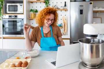 A young woman learns to cook, she watches video recipes on a laptop in the kitchen and cook a dish . Cooking at home concept