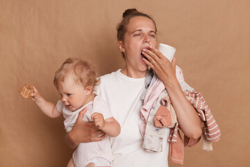 Portrait of sleepy overworked woman wearing white T- shirt holding her baby daughter in hands...