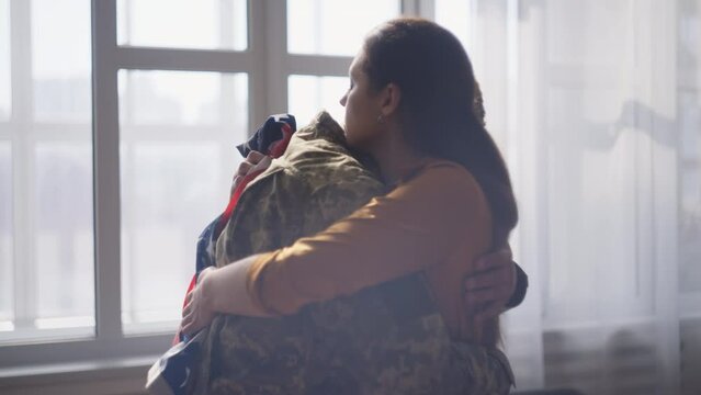 Sad woman with US flag hugging military man, farewells before leaving for war