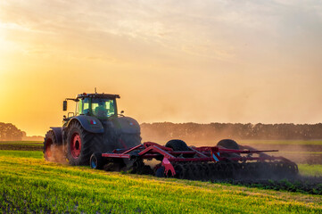 tractor in the field under sunset light, tillage in spring, preparation for sowing. High quality photo - obrazy, fototapety, plakaty