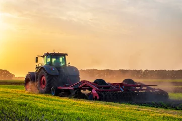 Fotobehang Tractor tractor in the field under sunset light, tillage in spring, preparation for sowing. High quality photo