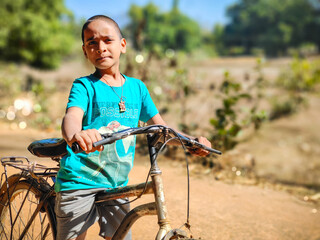 Boy with his bike standing against the blue sky and green forest, Selective focus Copy space