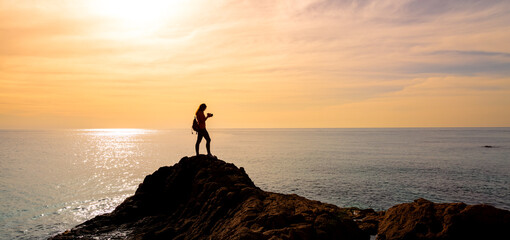 silhouettte of woman photographer taking photo on sunset at the sea