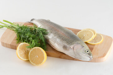 Raw trout on a wooden cutting board with sliced lemon and fresh dill