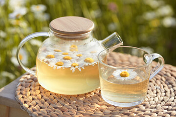 Close-up glass teapot with a mug of aromatic chamomile tea on nature background