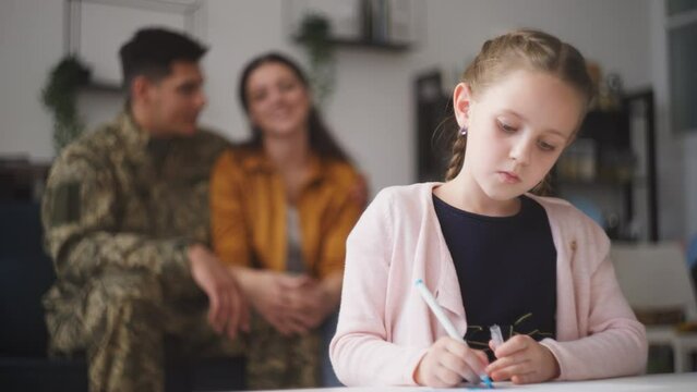 Loving military father and mother admiring little daughter drawing picture