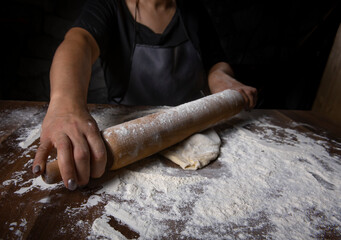 Chef is rolling the dough with the rolling pin on the on the table. Hands close-up.Cooking pasta, bread, spaghetti, khachapuri, food concept