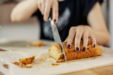 Close up of a woman cutting a bread at home with knife.