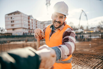 A happy site worker is shaking hands with site manager while standing at site.