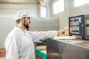 A meat industry worker is pressing butting on dashboard on a meat processing machine.