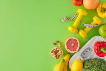 Slimming concept. Flat lay composition made of scales, dumbbells and tape measure, nuts, vegetables and fruits on green background with copy space. Proper diet idea.
