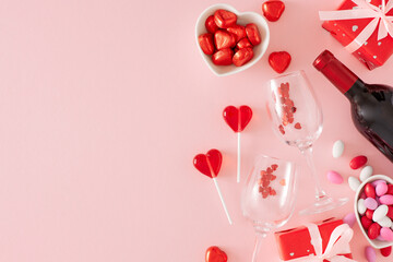 Valentines Day concept. Flat lay composition made of gift box, wine bottle with glasses, saucers with chocolate candies and lollipops on pink background with copy space. Sweet Valentines card idea.