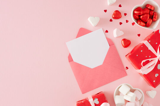 Valentines Day concept. Flat lay photo of red gift boxes, envelope with letter, heart shaped saucers with chocolate candies and marshmallow on pastel pink background with copy space. - Powered by Adobe