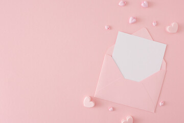 Valentines Day concept. Flat lay photo of envelope with letter and pink heart shaped baubles on pastel pink background with copy space. Women's day celebration idea.