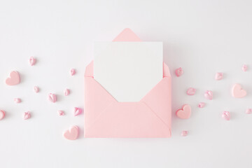 Valentines Day concept. Flat lay photo of pink heart shaped baubles on white background and envelope with letter in the middle. Lovers holiday card idea.