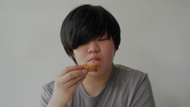 Asian fat boy eating delicious fried chicken, wearing a grey t-shirt. Concept child health problems, Pathogenic junk food.