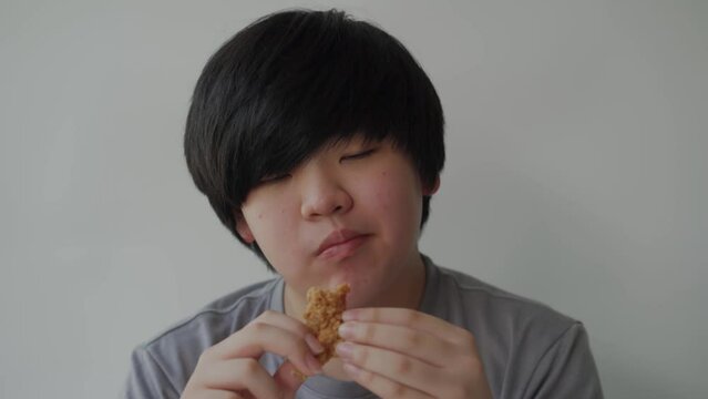 Asian fat boy eating delicious fried chicken, wearing a grey t-shirt. Concept child health problems, Pathogenic junk food.