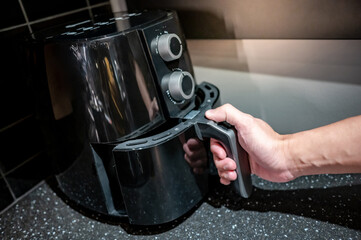 Male hand holding an electric air fryer handle in the kitchen. Home appliance for healthy cooking lifestyle.