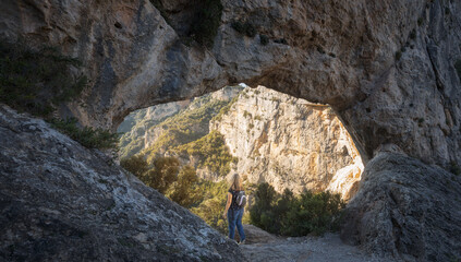 Fototapeta na wymiar Woman Looking Through the Natural Arch Forat de la Vella at Ports de Beseit Natural Park, Catalonia