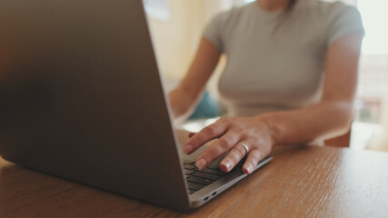 Fototapeta premium Close-up of young woman's hands typing on laptop while sitting at home